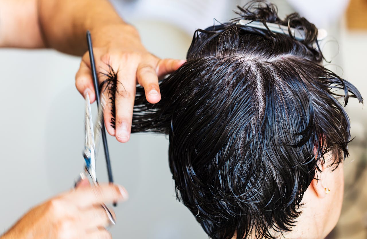 about-01 Close-up of a stylist cutting dark, wet hair in a salon setting, showcasing the precision and technique of hairstyling.