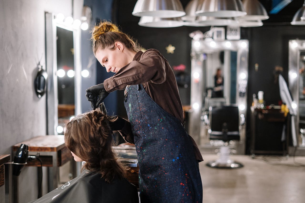 hero-img-02 A female stylist expertly applying hair color to a client in a modern salon setting.